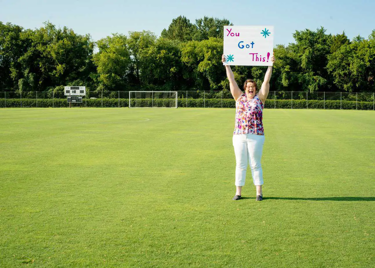 Tonya Lawson standing on a soccer field holding a sign that say you got this!