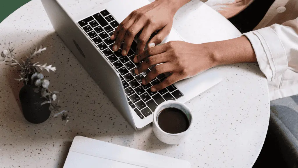 Hands typing on a computer about why you need a blog. a cup of coffee is sitting on the table to the left of the laptop