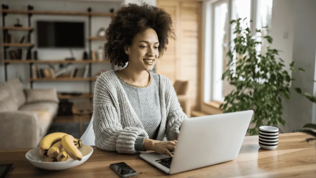 woman sitting at a table typing on a laptop. She's starting a blog
