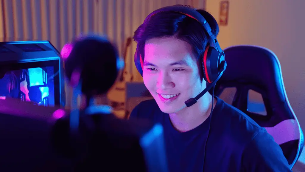 college student earning passive income by live streaming on twich.  He is wearing a gaming headset and looking at the computer. 