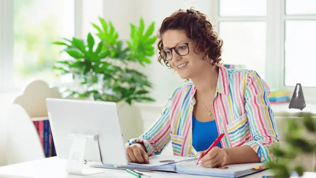 Music teacher sitting at a desk working on her blog. there is a green plant and a metronome in the background